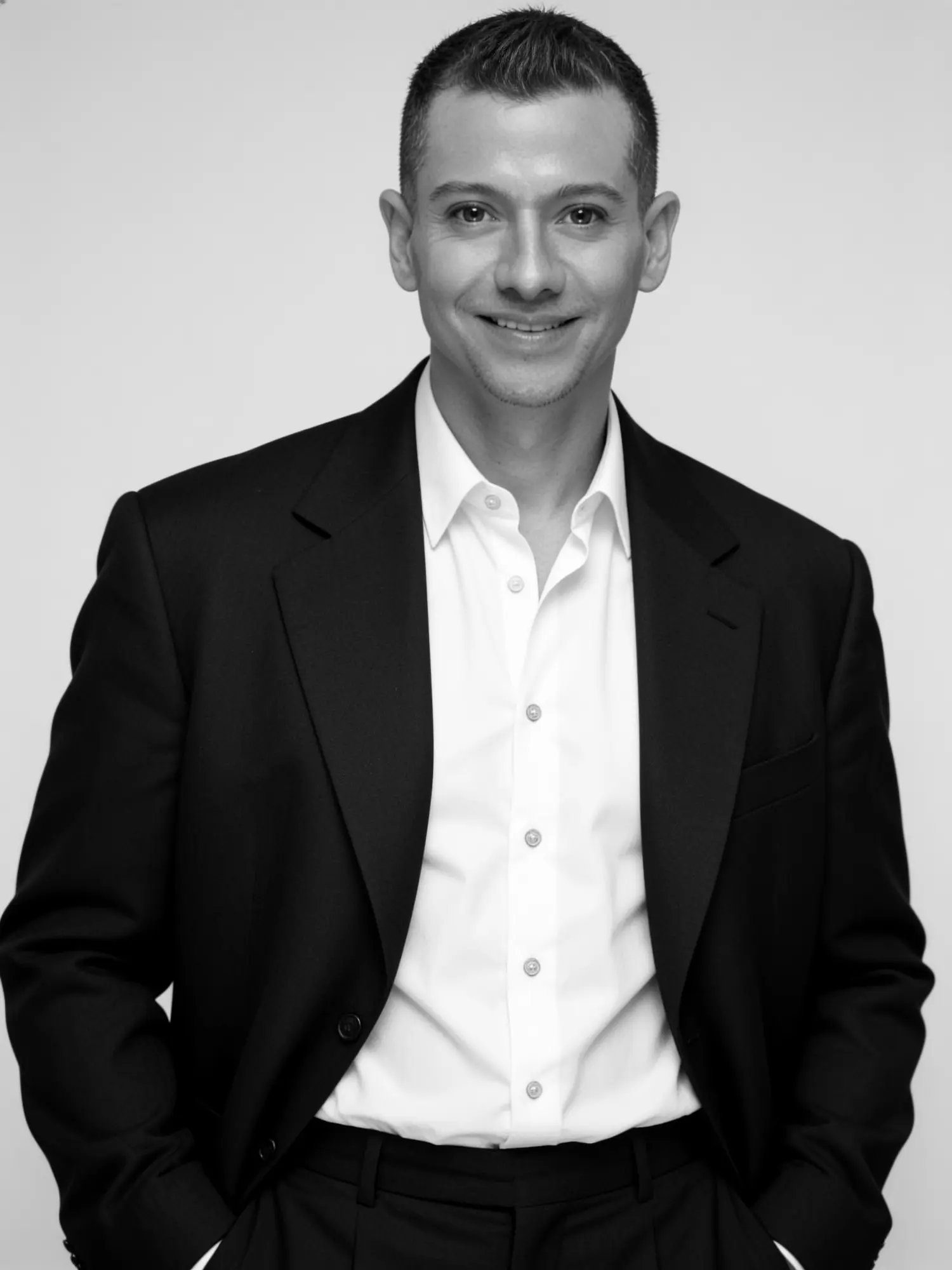 Black-and-white portrait of Francisco Lugo standing and smiling, in a dark blazer and white shirt with his hands in his pockets.