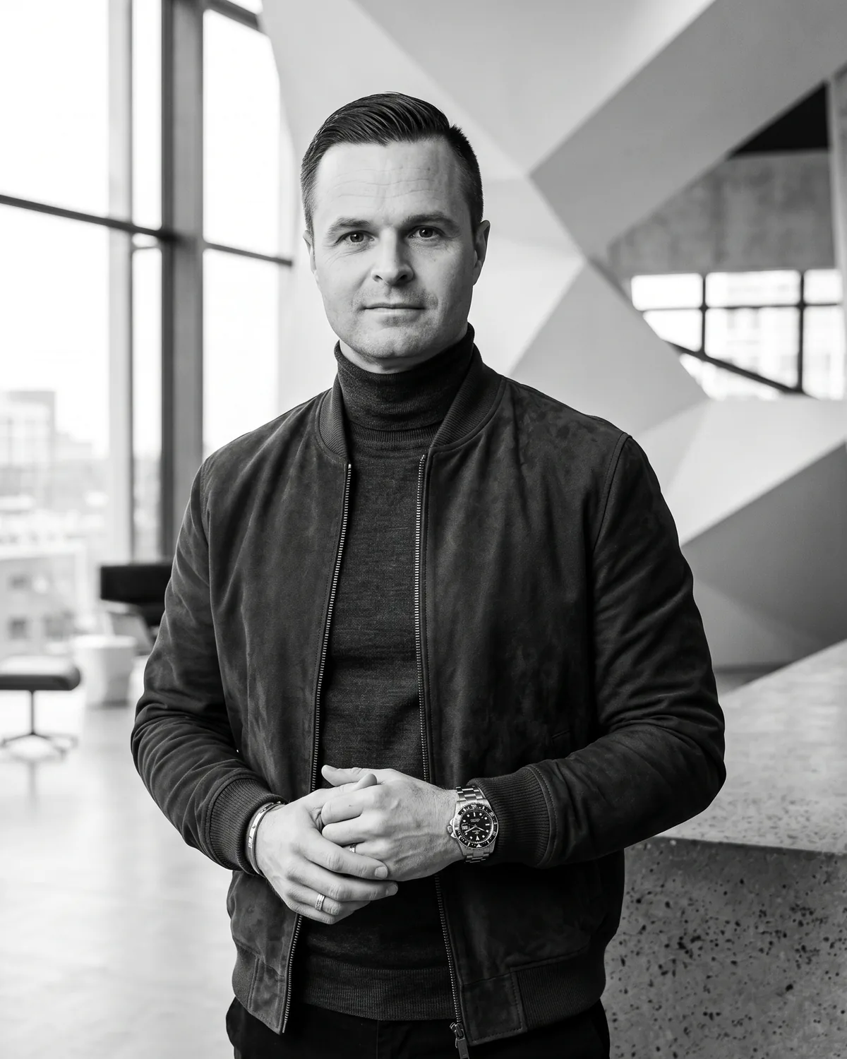 Portrait of Maciej Adamski in a dark jacket and turtleneck in a modern interior, in black and white.