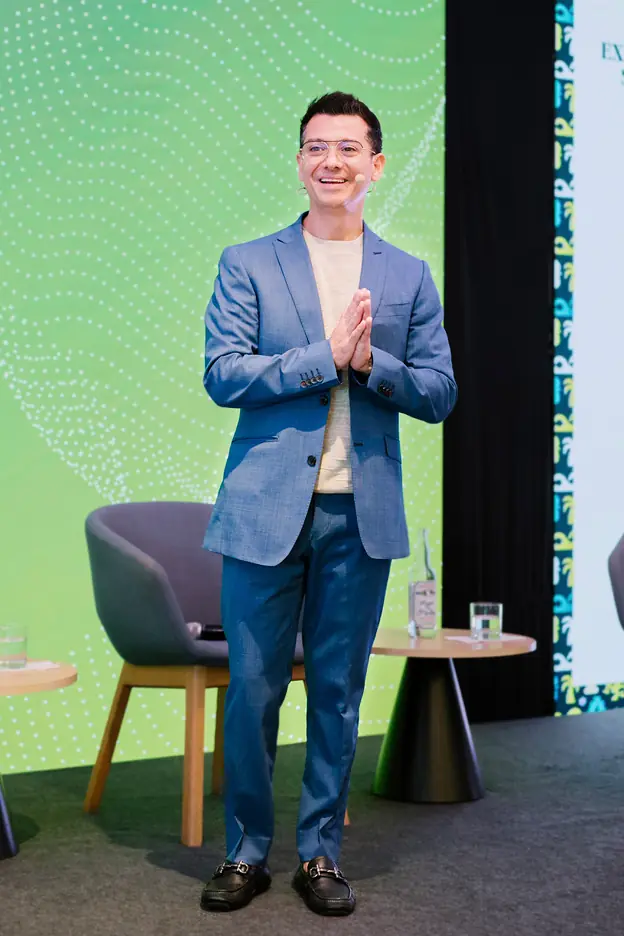 Francisco Lugo on stage at a hospitality event, smiling with his palms pressed together.