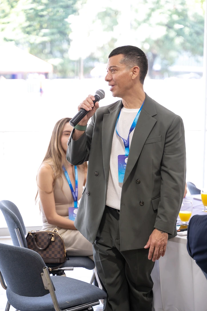 Francisco stands with a microphone beside a seated participant.