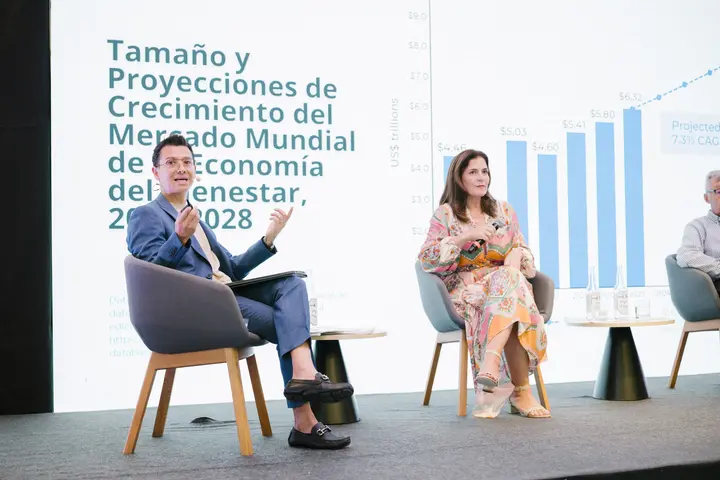 Francisco speaks, seated on stage at Summit Mexicano de la Hospitalidad, in front of a chart of wellness market growth.