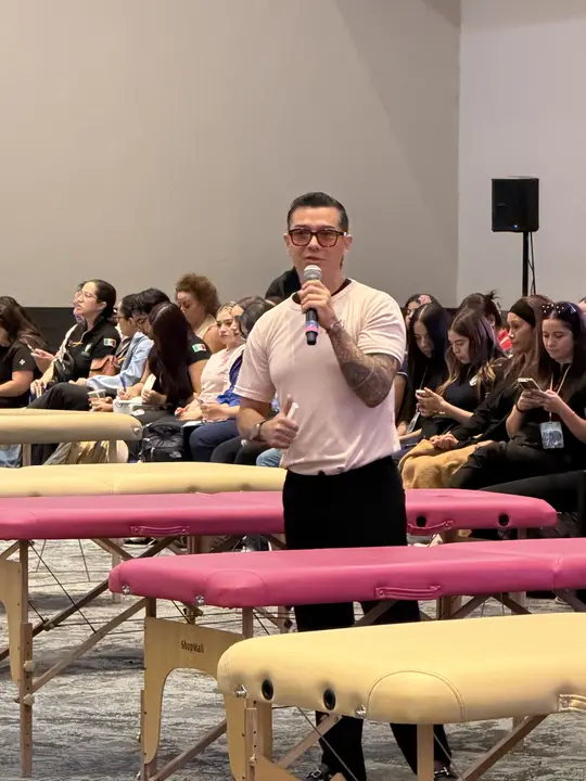 Francisco speaks into a microphone to the audience, among massage tables, at The Therapist of Today talk.